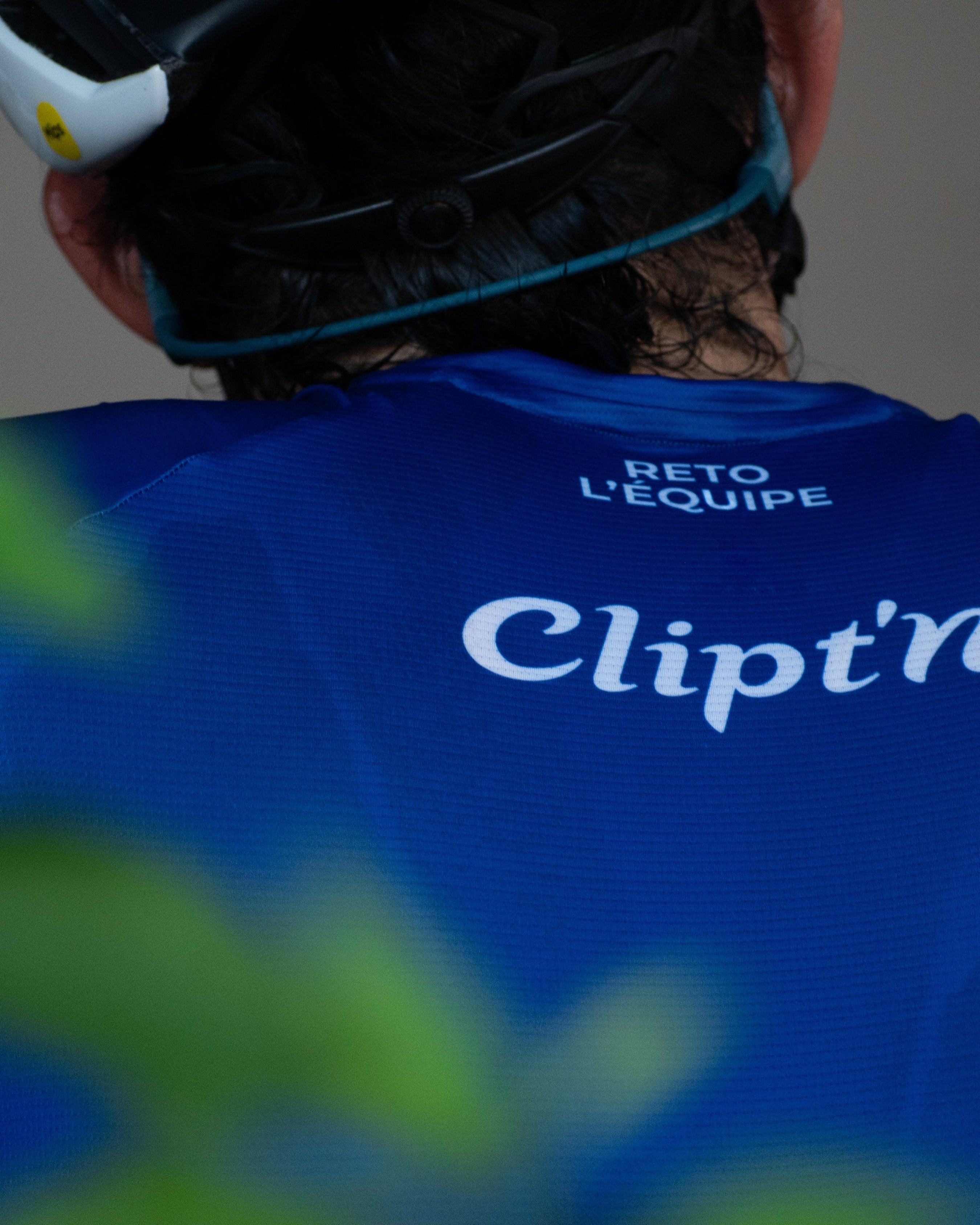 Person wearing a blue cycling jersey with 'Clipt'n' branding, looking over their shoulder.