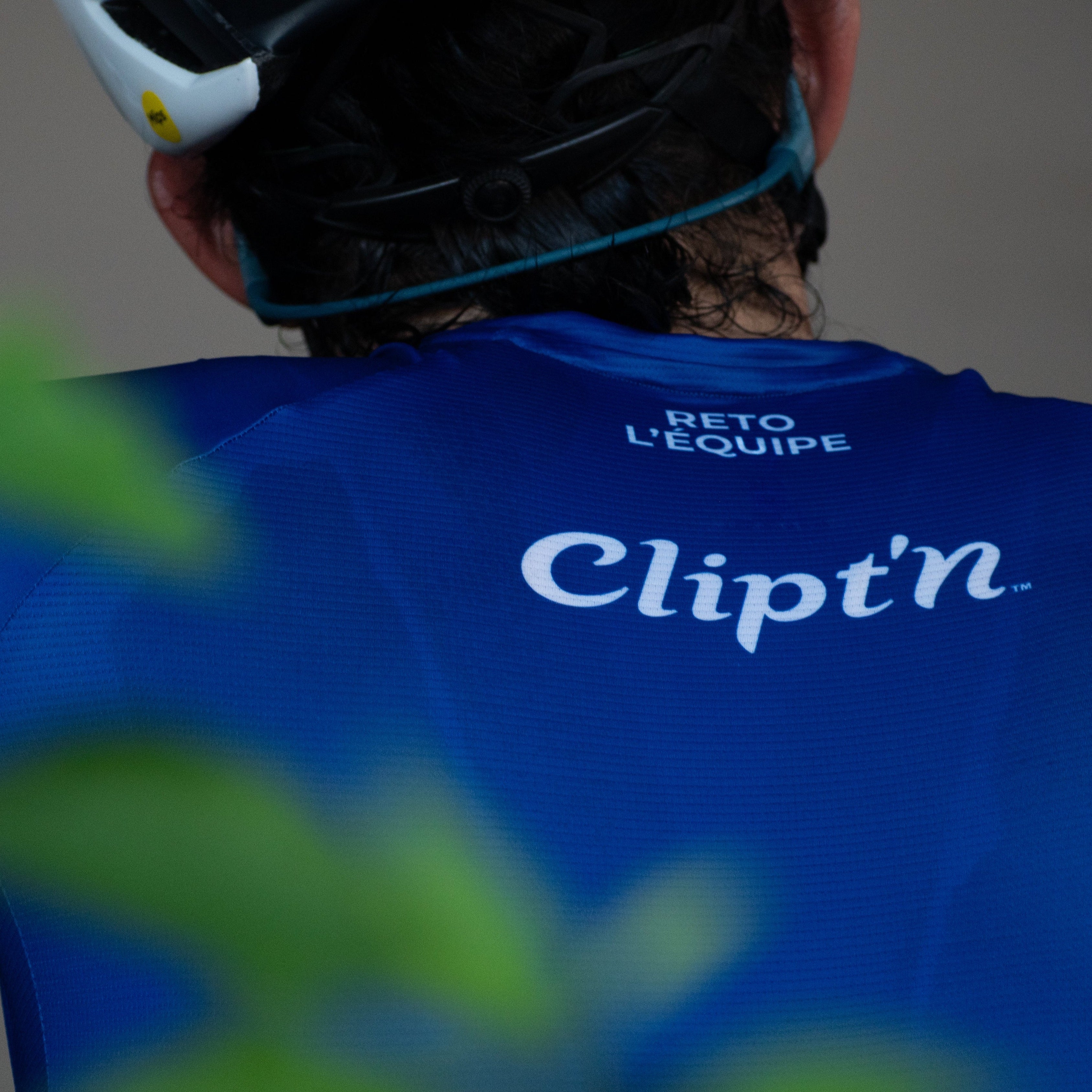 Person wearing a blue cycling jersey with 'Clipt'n' branding, looking over their shoulder.