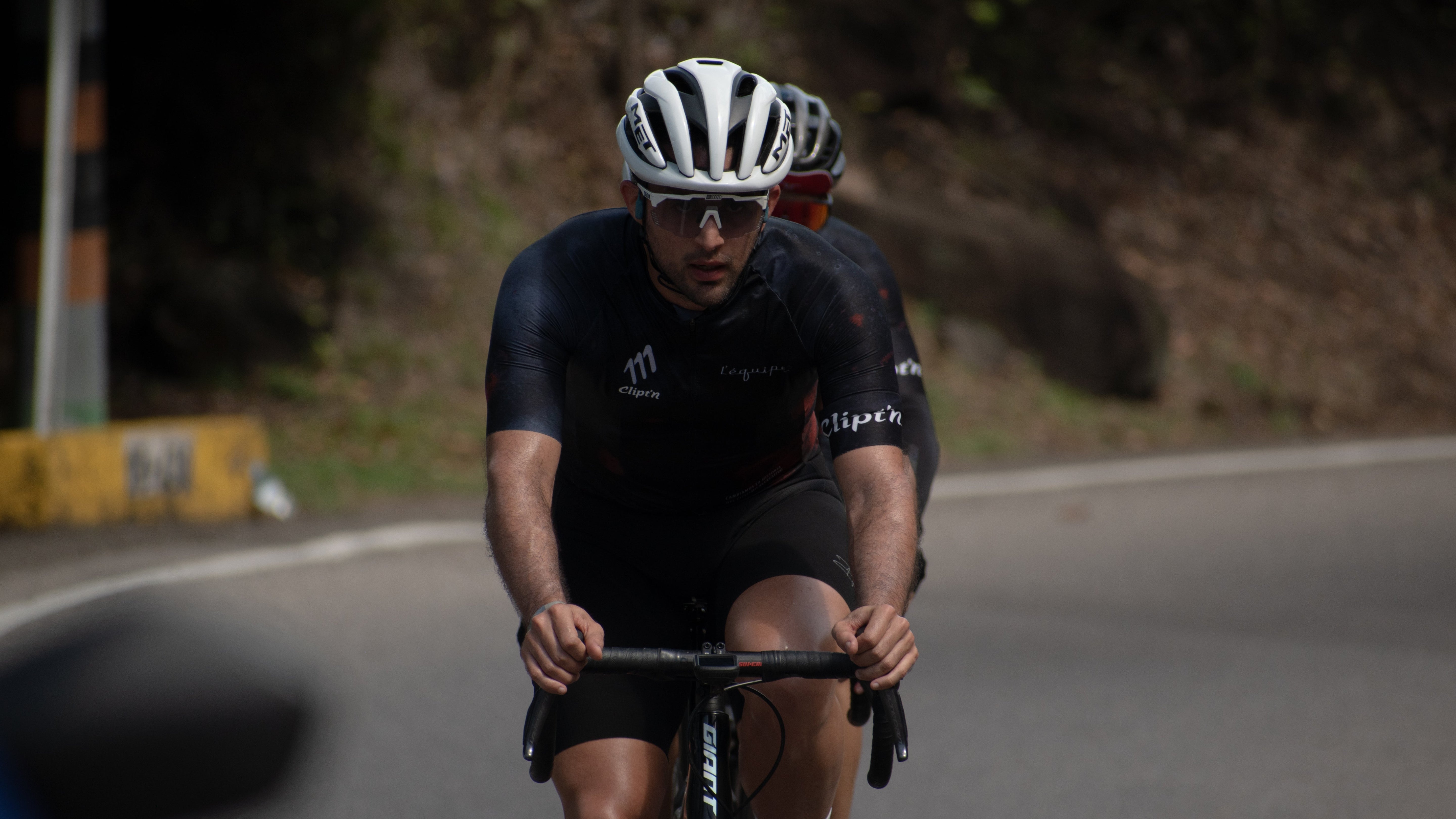 Two cyclists in black uniforms riding on a road with blurred background